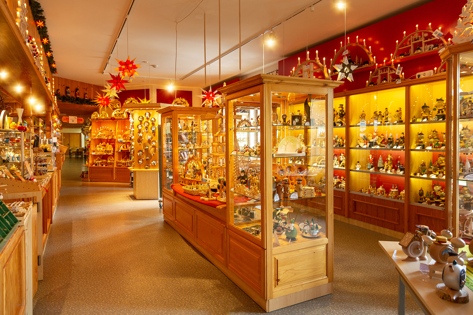 Ein Nussknacker König mit schwarzer Krone weißem Bart und roter Uniform steht auf einem Tisch Im Hintergrund sind weitere Nussknacker und verschwommene Werkstatt sichtbar